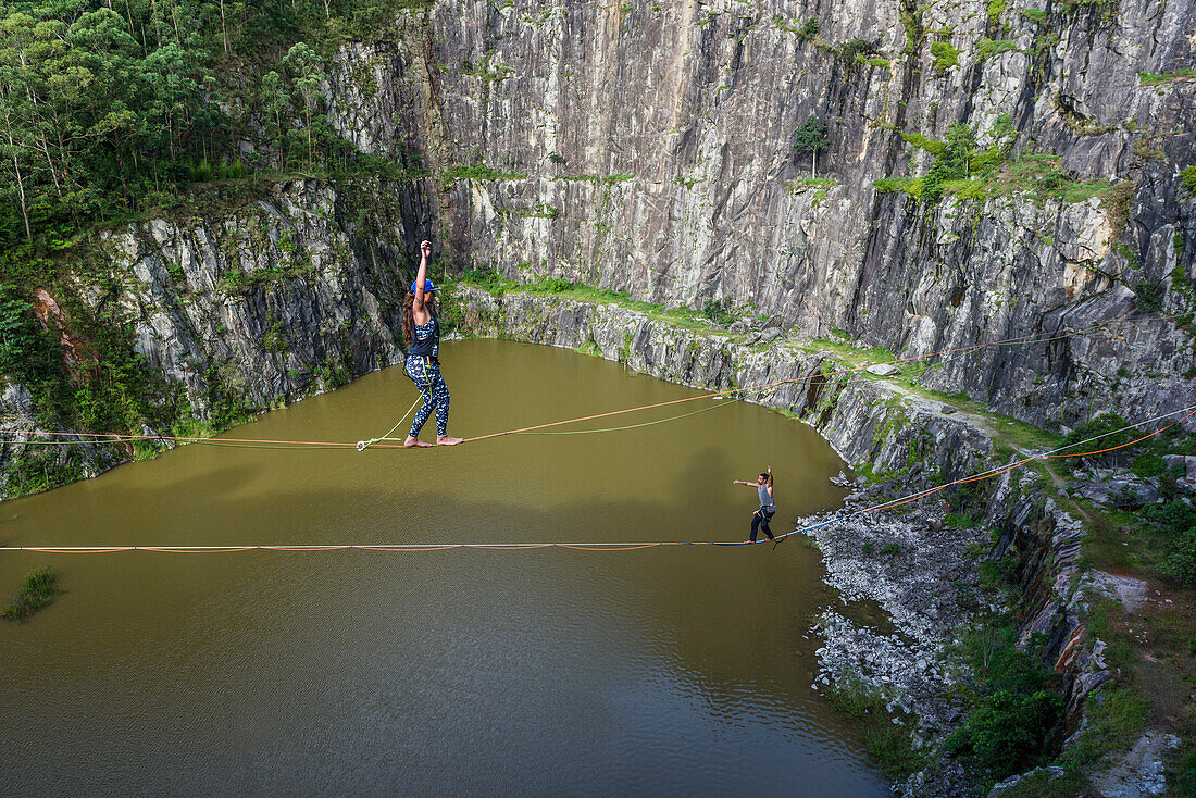Adventurous man and woman crossing quarry in opposite directions on separate slacklines, Dibs Quarry, Maripora, Sao Paulo State, Brazil