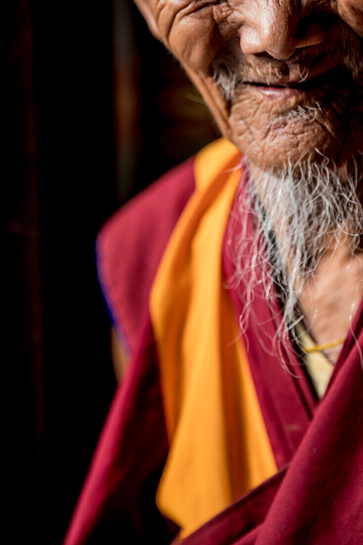 Mid section photograph of smiling senior Buddhist monk with white beard, Boudhanath Temple, Kathmandu, Nepal