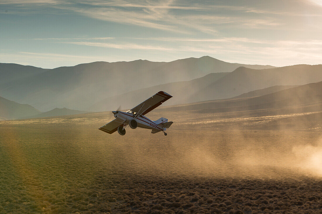 A prop plane leaves behind a dust cloud after takeoff.