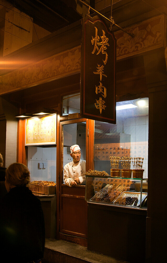 Vendor in chefs hat at food shop at night market, Beijing, China