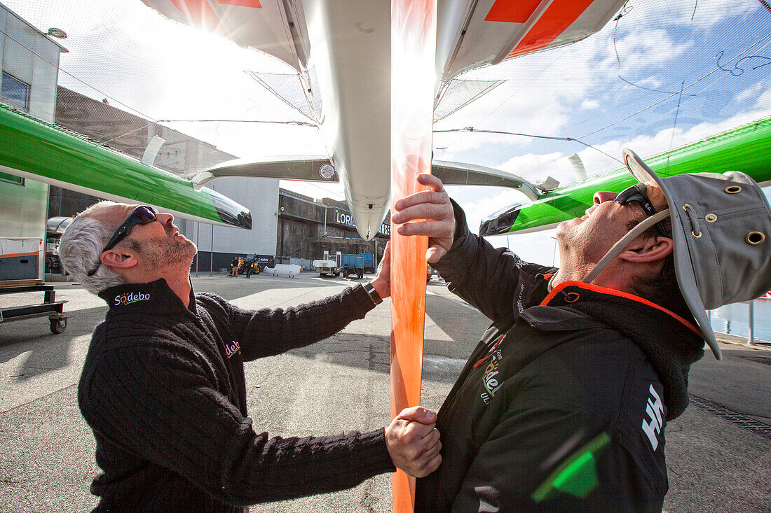 Two sailors installing central rudder on trimaran before being relaunched, Lorient, Brittany, France