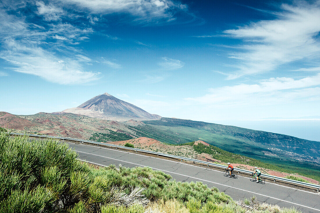 Two cyclists pedaling on mountain road with Mount Teide in background, Teide National Park, Tenerife, Canary Islands, Spain