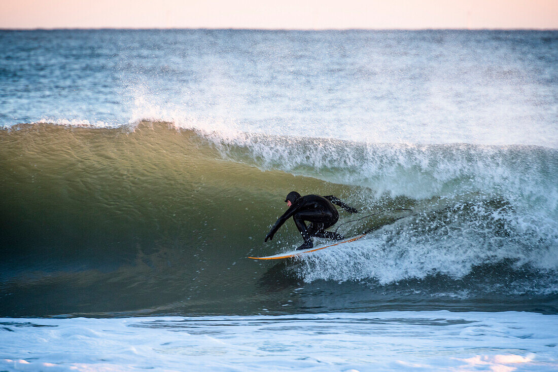 Full length shot of surfer in wetsuit riding wave in sea