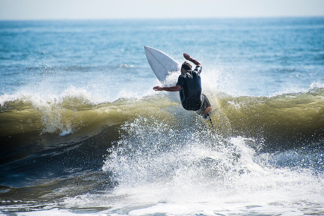 Rear view of surfer in wetsuit riding wave in sea