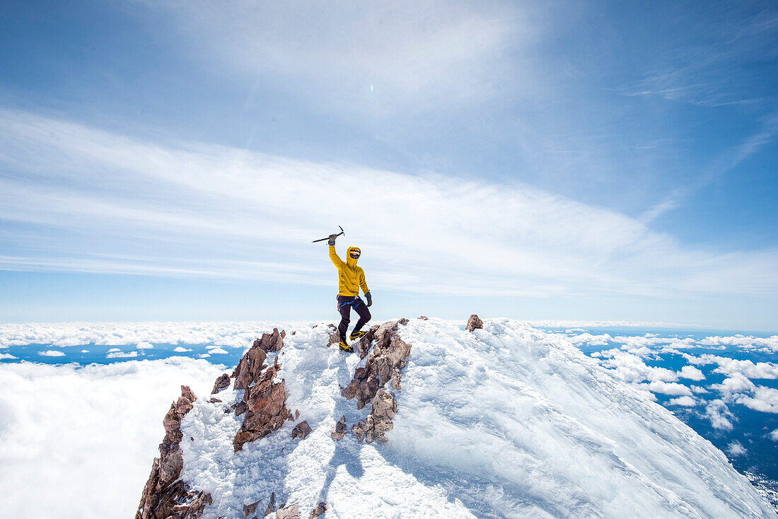 Adventurous mountain climber rising ice pick in victory pose at summit of Mt Shasta, California, USA
