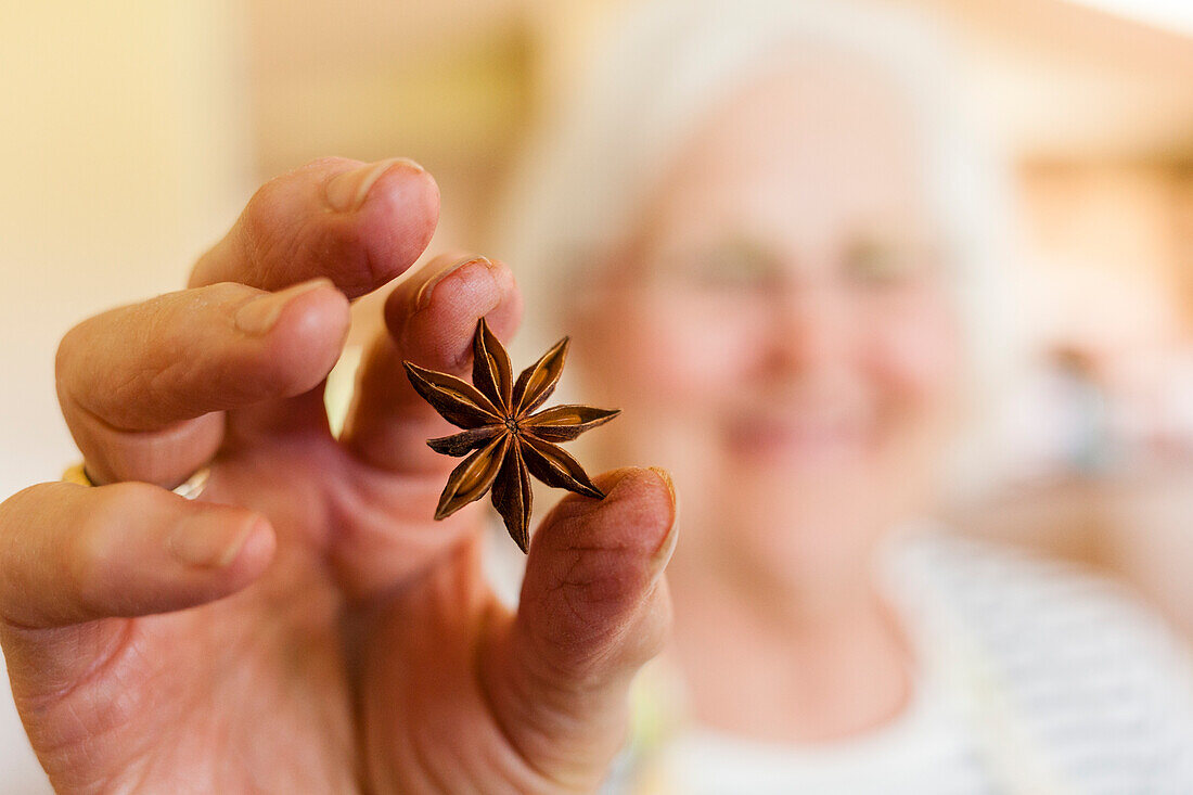 Smiling senior woman holding Anise Star which is used in cooking, Fort Collins, Colorado, USA