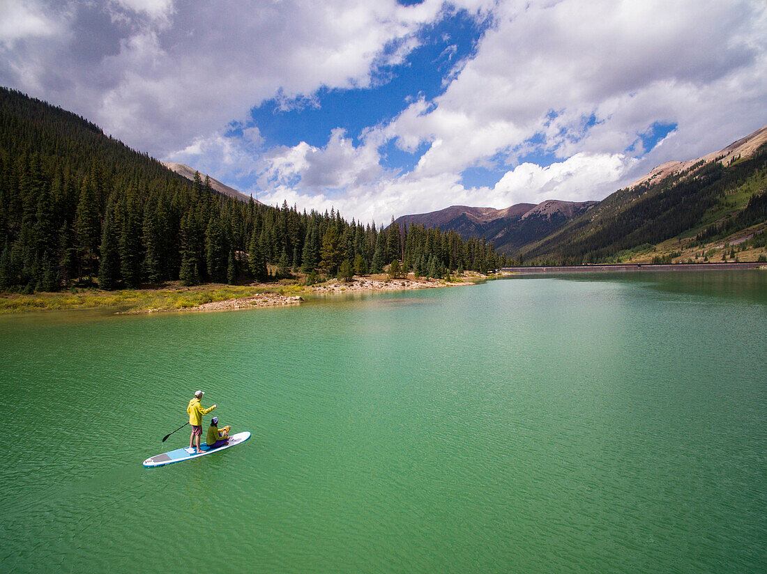 Couple paddling with their dog on paddle board at reservoir in mountains near Aspen, Colorado, USA