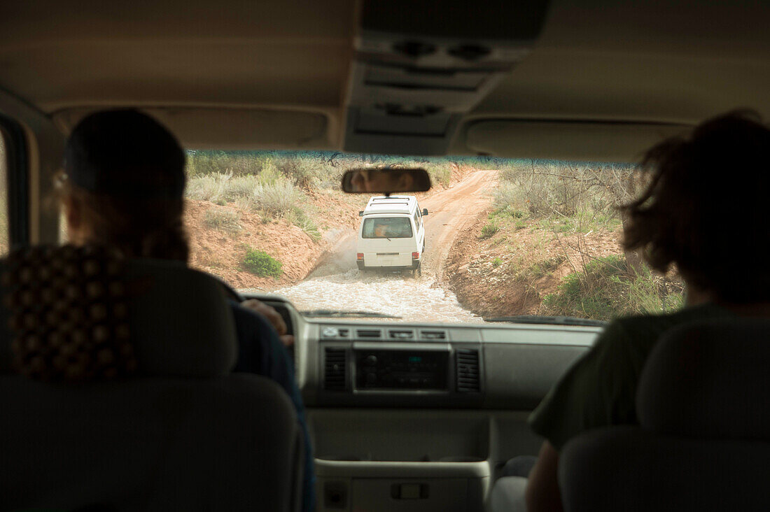 Rear view of two men driving down dirt road to go rock climbing, Moab, Utah, USA
