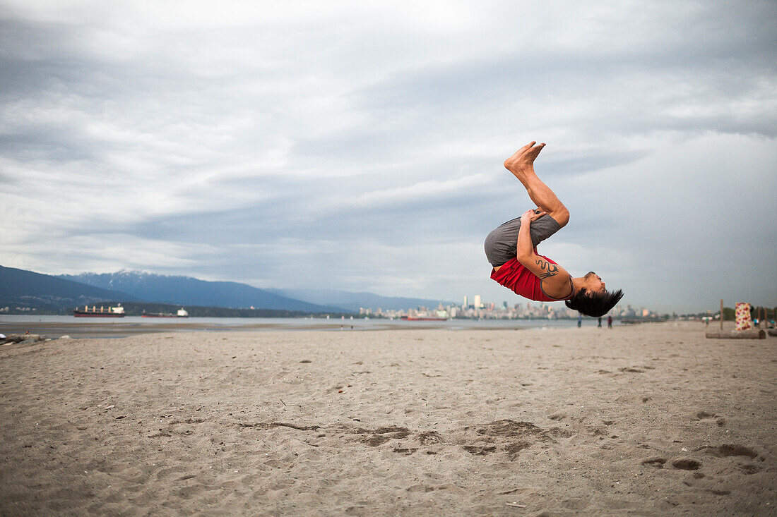 Man doing backflip in mid-air while doing acroyoga at beach