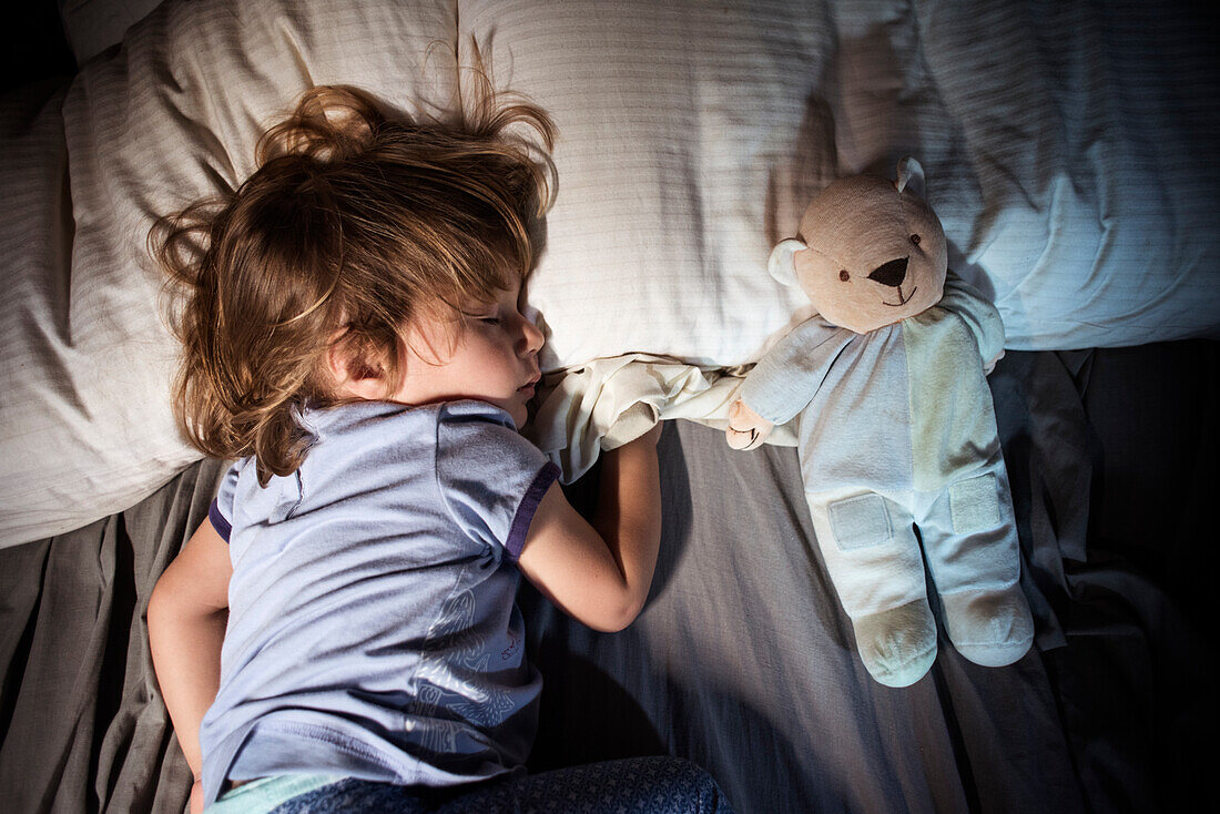 Overhead view of young girl sleeping with teddy bear in bed