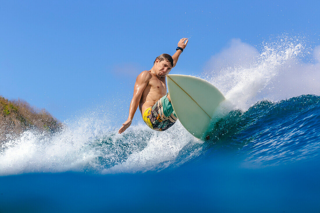 Young man riding wave on surfboard in sea