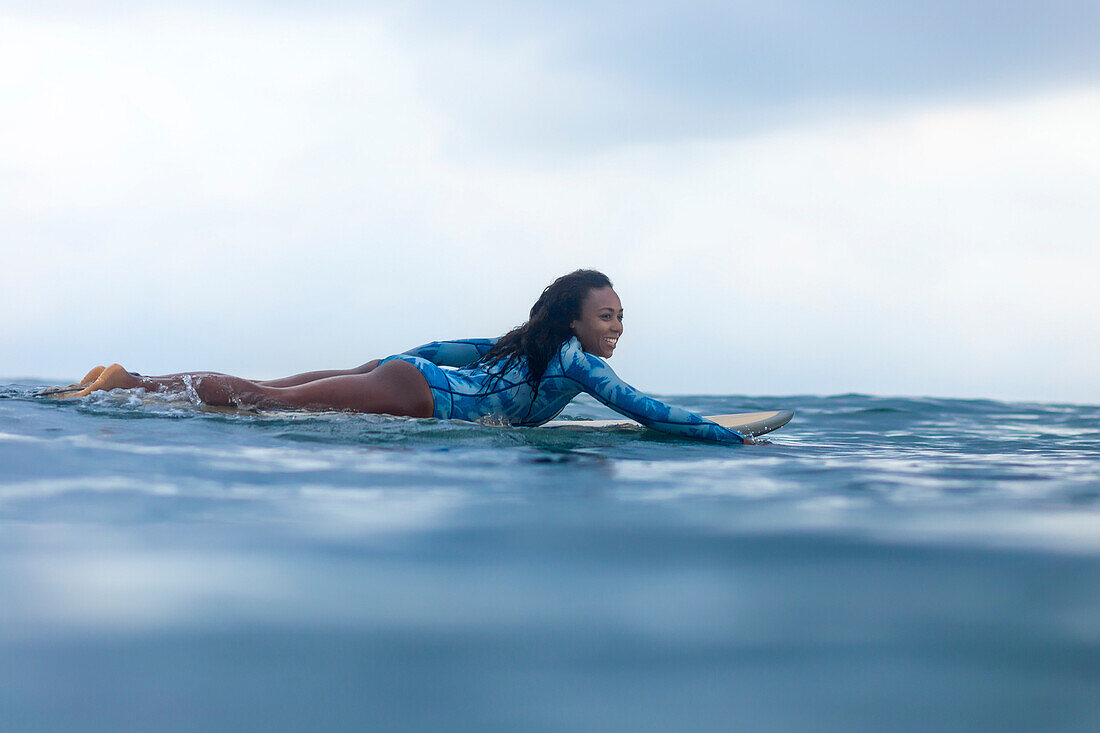 Side view shot of woman paddling on surfboard in sea