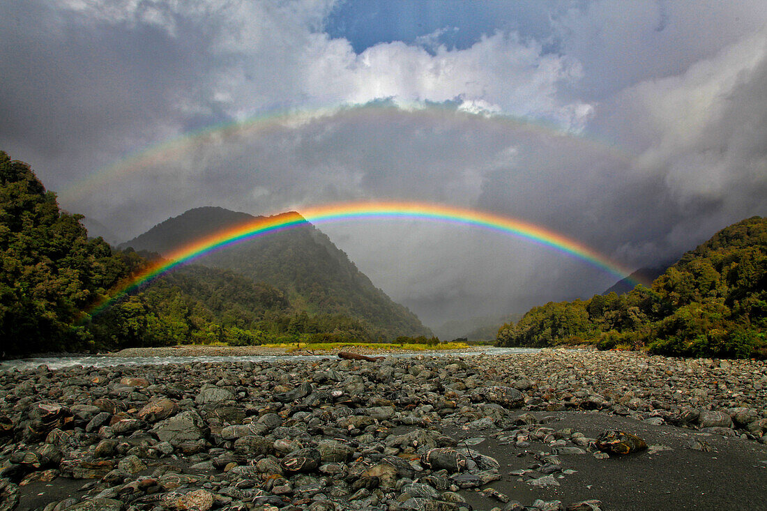 Double rainbow against large clouds over rocky valley, New Zealand