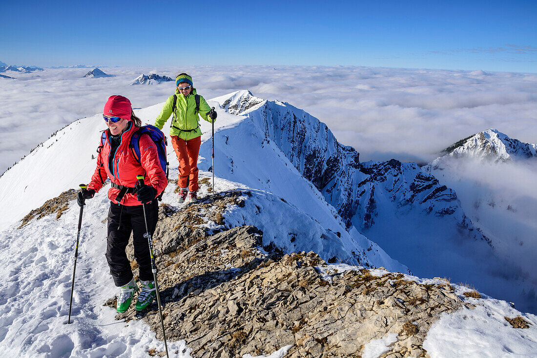 Two women backcountry skiing ascending towards Hinteres Sonnwendjoch, fog in the valley, Hinteres Sonnwendjoch, Bavarian Alps, Tirol, Austria