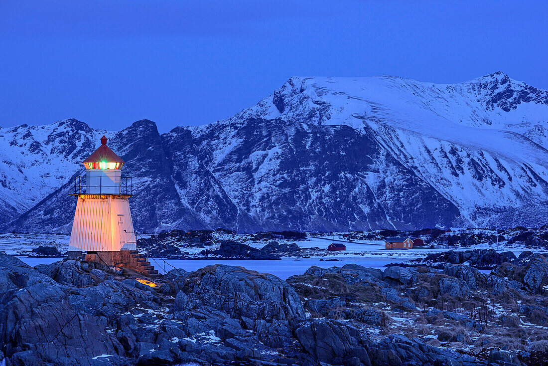 Leuchtturm von Gimsoy in der Dämmerung mit verschneiten Bergen im Hintergrund, Lofoten, Nordland, Norwegen