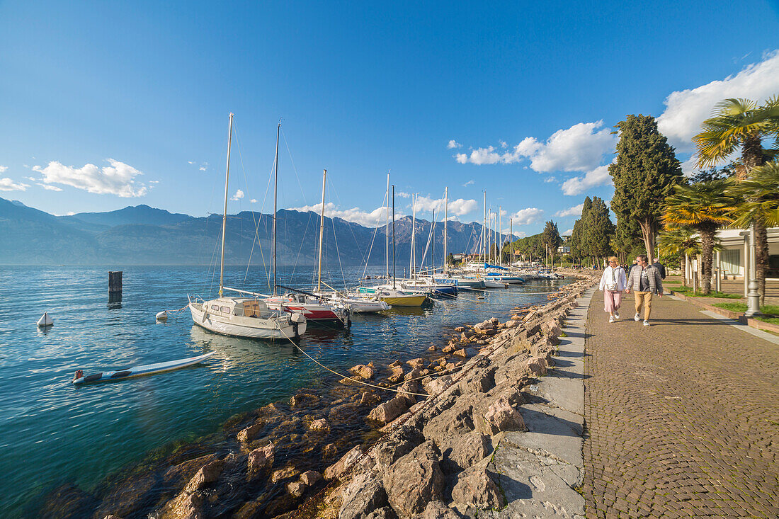 Tourists walking along the lakefront of Malcesine on the eastern shore of Lake Garda, Verona province, Veneto, Italy.