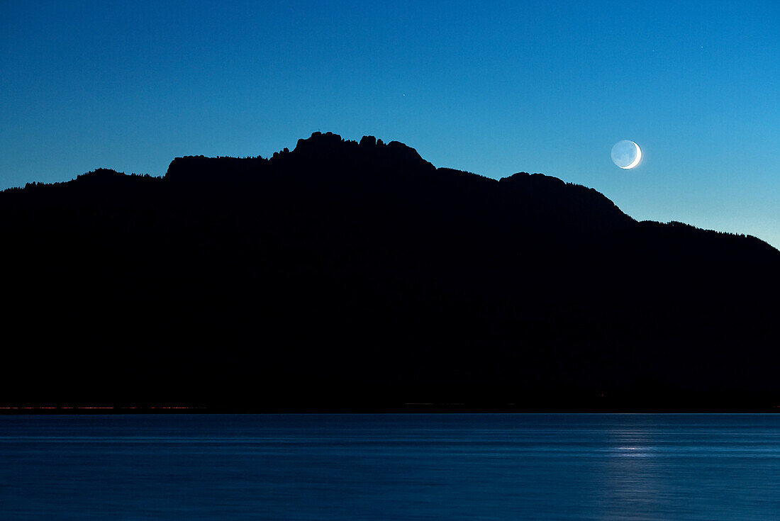 Car tail lights as light strips in front of the Kampenwand on Lake Chiemsee, the moon shines