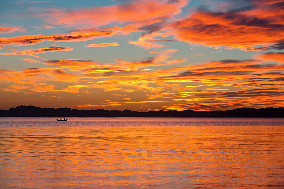 Angler mit kleinem Motorboot im letzten Abendlicht beim Sonnenuntergang am Chiemsee, dramatische Farb- und Wolkenstimmung
