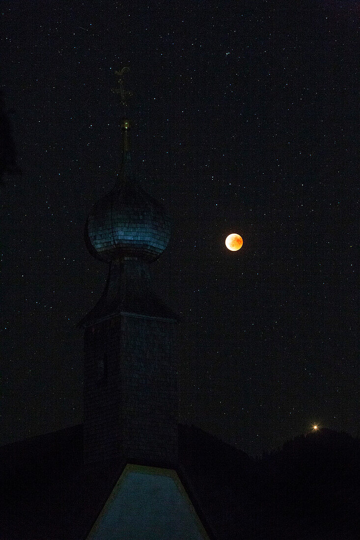 blutroter Mond bei der Mondfinsternis 2018; im Vordergrund der Zwiebelturm der Kirche von Almau bei Übersee