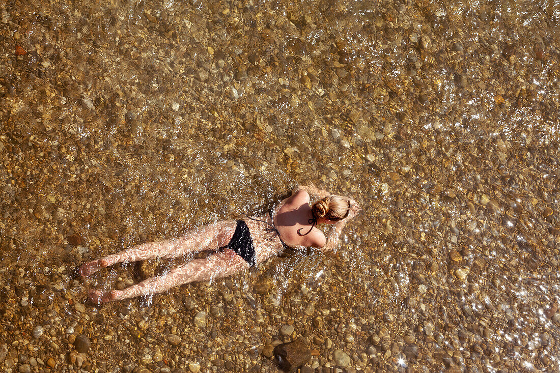 junge Frau mit schwarzem Bikini liegt im Flachen Wasser der Isar am Flaucher, Blick von oben