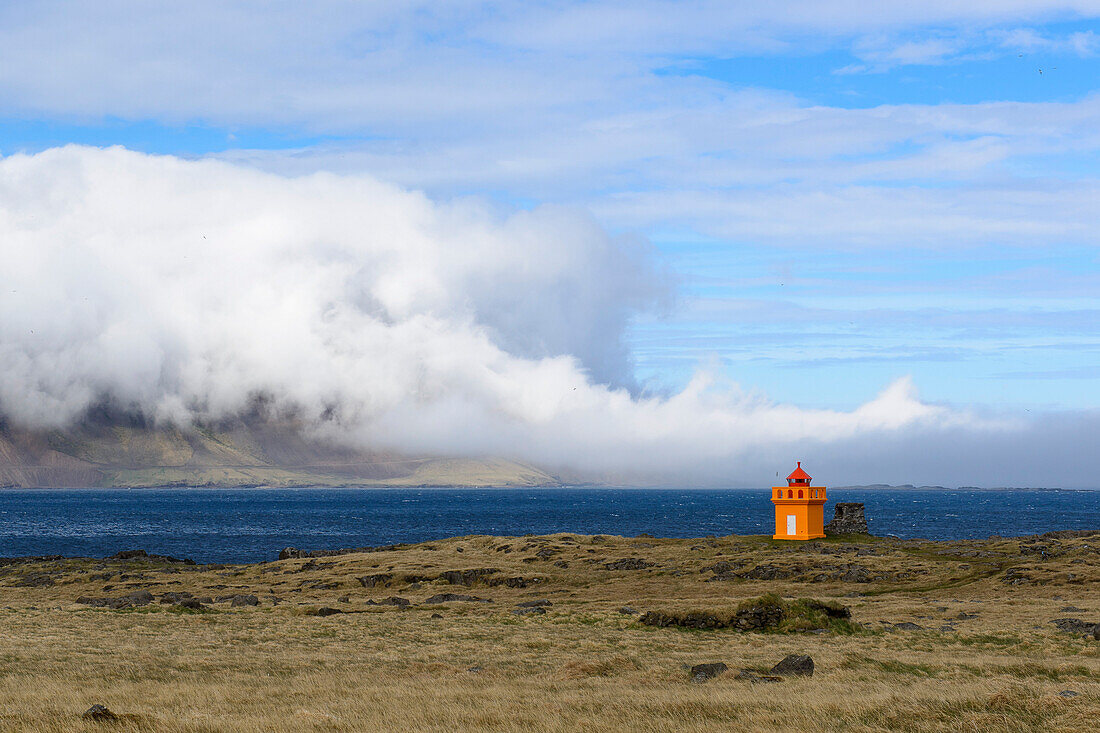 Kleiner orangener Leuchtturm und Seenebel an den Ostfjorden Islands