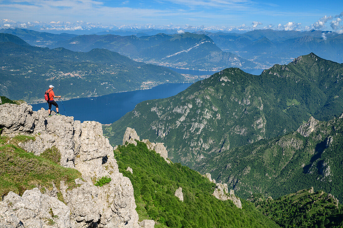 Man hiking standing at ledge and looking towards lake lago di Como, from Grignetta, Grigna, Bergamasque Alps, Lombardy, Italy