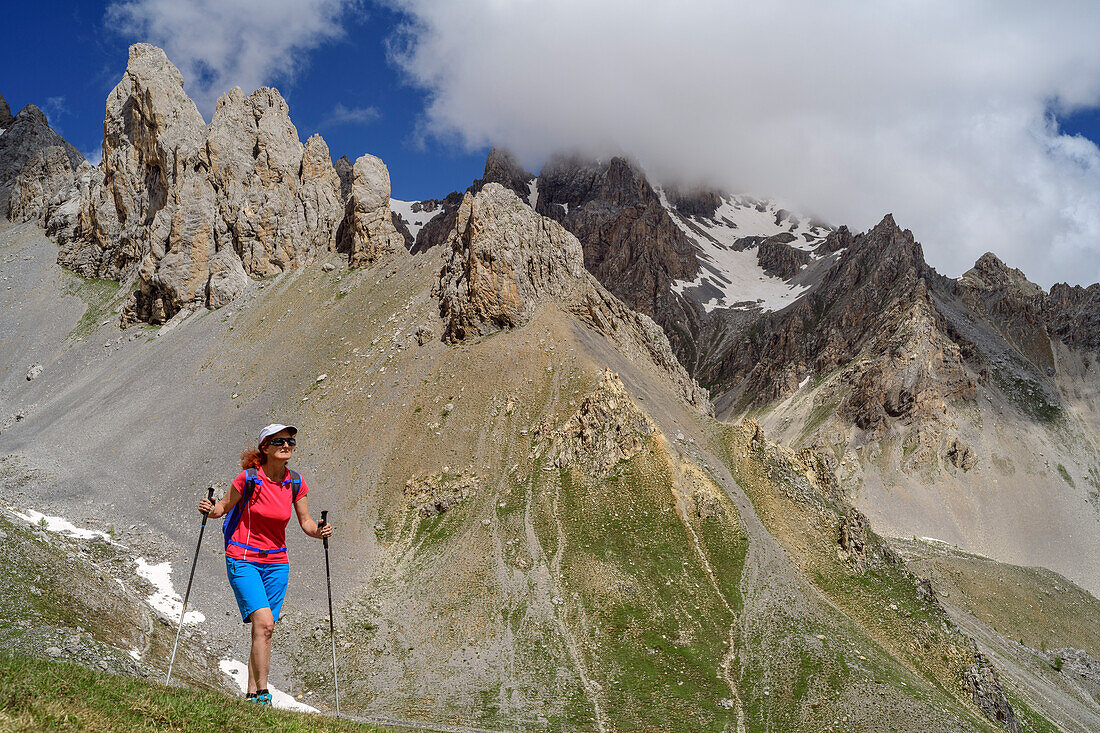 Frau beim Wandern mit Felstürmen im Hintergrund, Passo della Cavalla, Val Maira, Cottische Alpen, Piemont, Italien