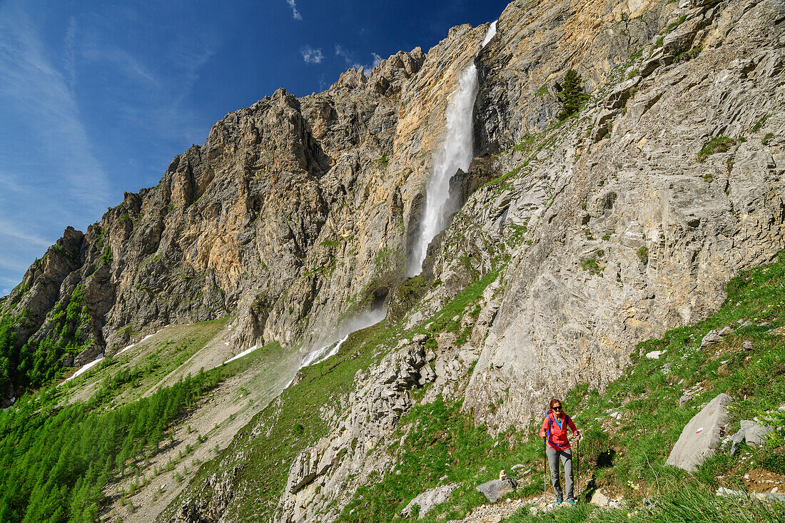 Woman hiking ascending towards hut rifugio Stroppia, waterfall cascata Stroppia in background, Val Maira, Cottian Alps, Piedmont, Italy