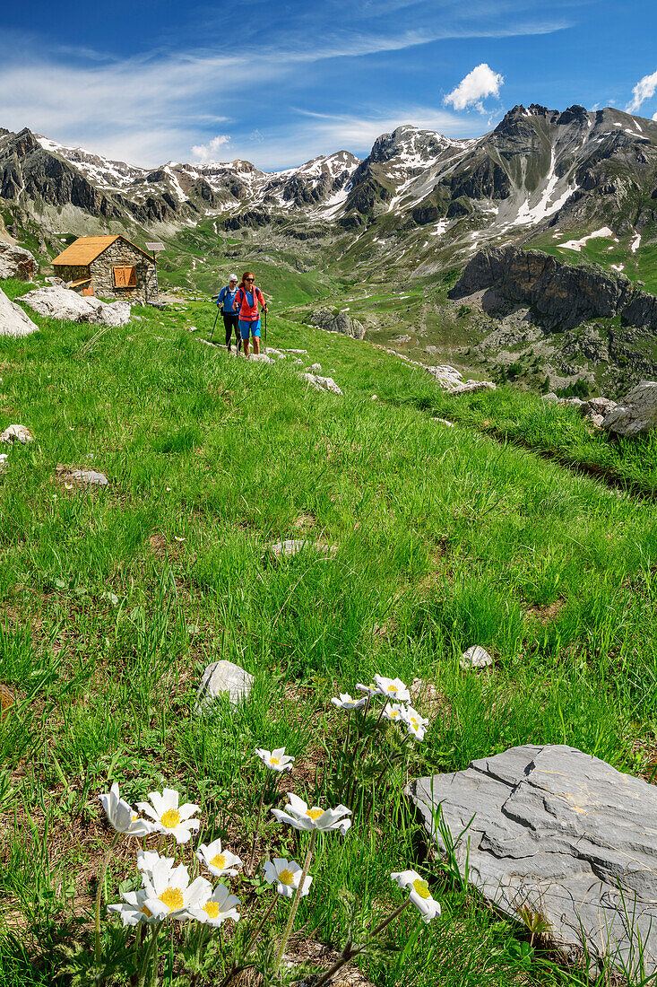 Man and woman hiking with hut rifugio Stroppia in background, hut rifugio Stroppia, Val Maira, Cottian Alps, Piedmont, Italy