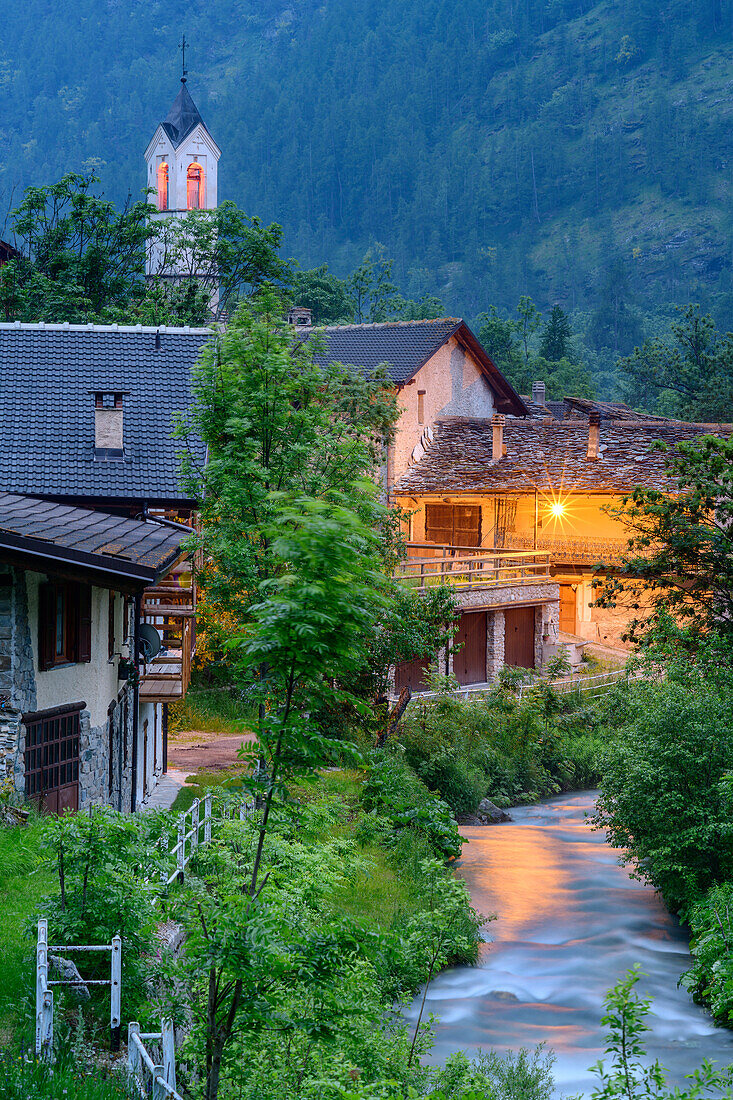 Alpine village with illuminated church and stream, Val Maira, Cottian Alps, Piedmont, Italy