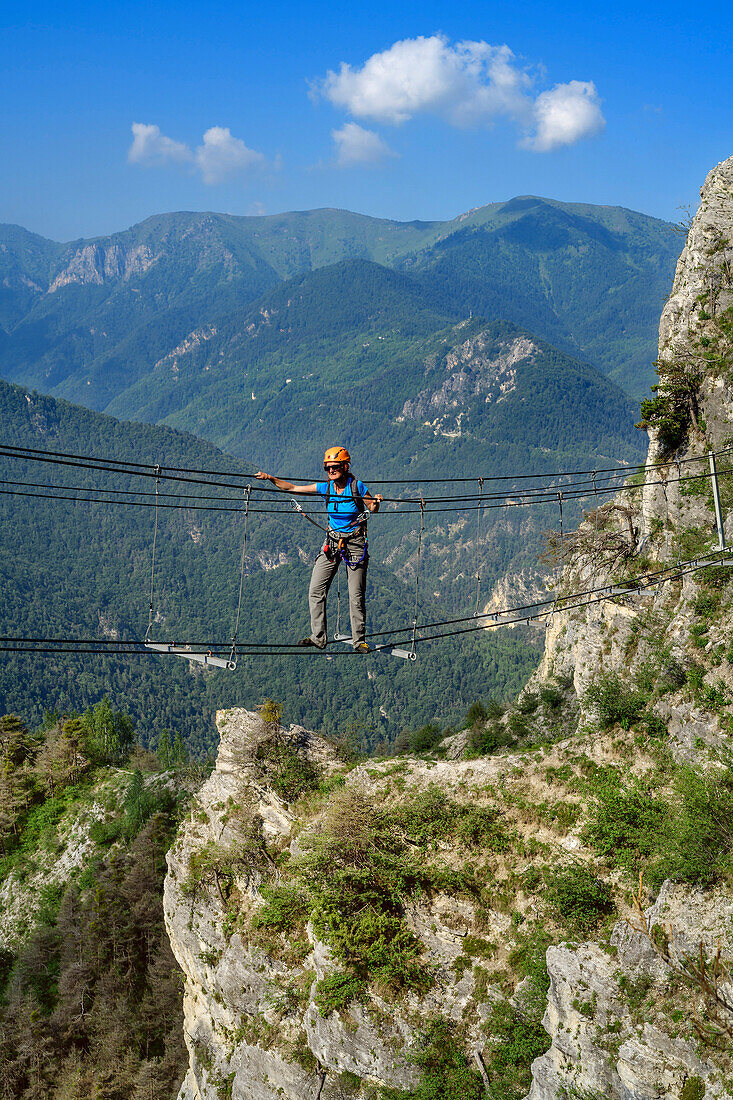 Woman climbing fixed rope route crossing ropeway, Ferrata di Camoglieres, Val Maira, Cottian Alps, Piedmont, Italy