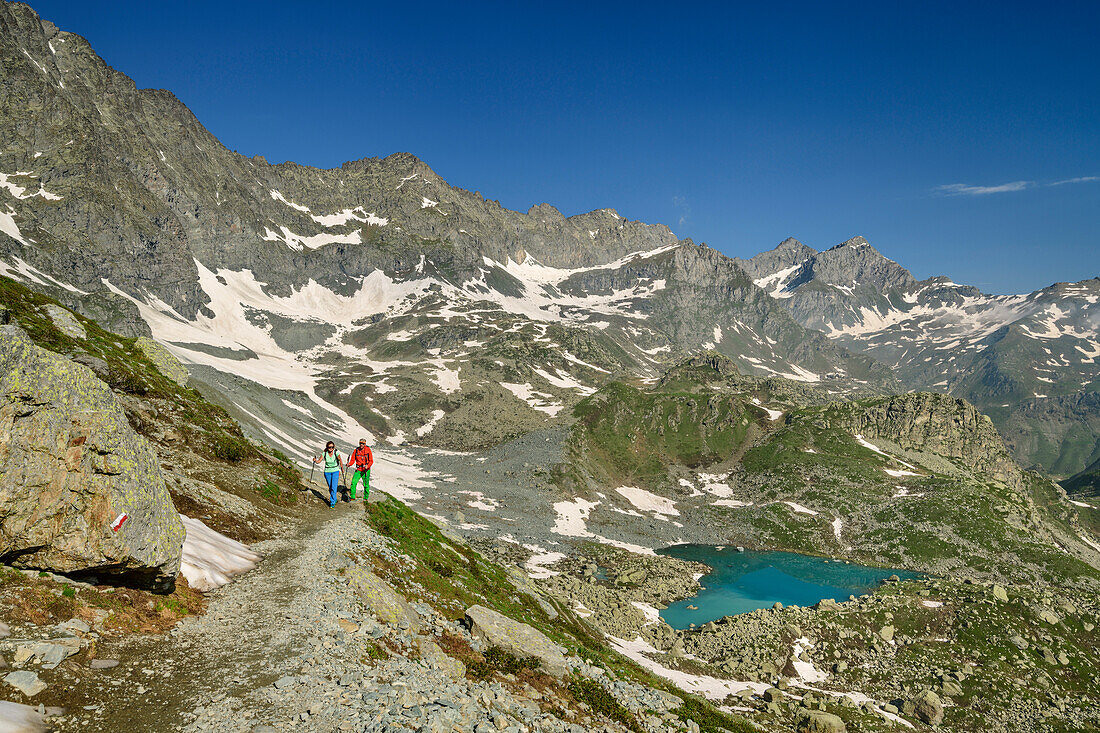 Man and woman hiking ascending from heart-shaped lake lago Chiaretto, Giro di Monviso, Monte Viso, Monviso, Cottian Alps, Piedmont, Italy