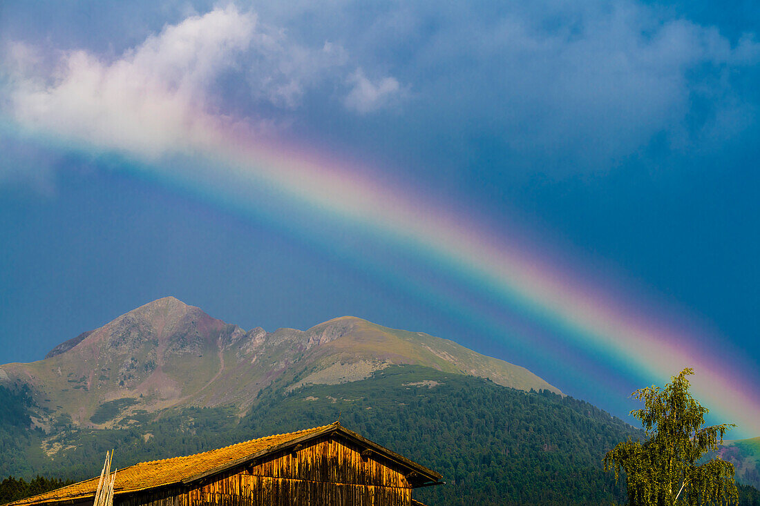 Wooden hut with Schwarzhorn mountains and rainbow, Radein, South Tyrol, Italy