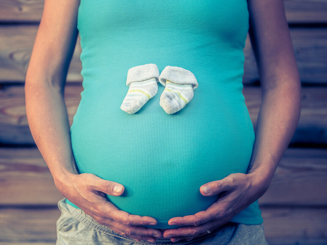 Kleine Babysocken auf dem Bauch einer Schwangeren