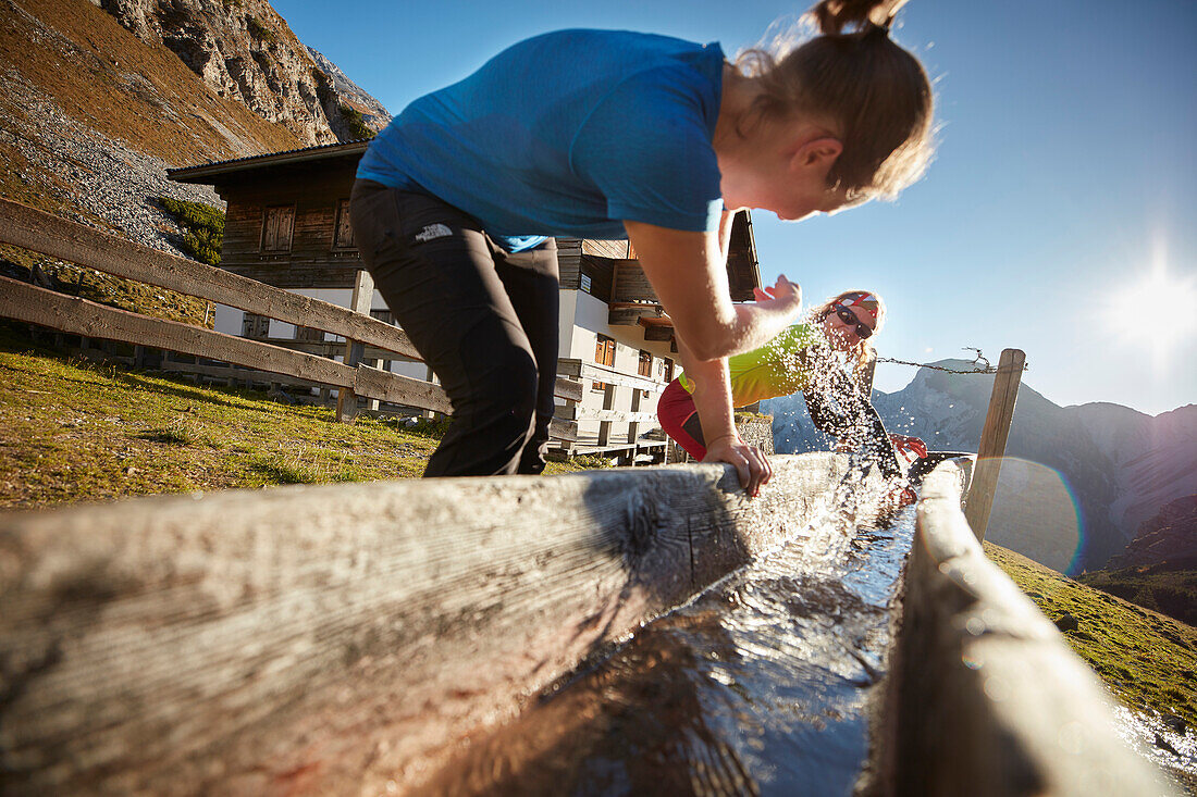 2 Wanderinnen spritzen Wasser aus Trog vor dem Gramaialm-Hochleger , Östliches Karwendelgebirge, Tirol, Österreich