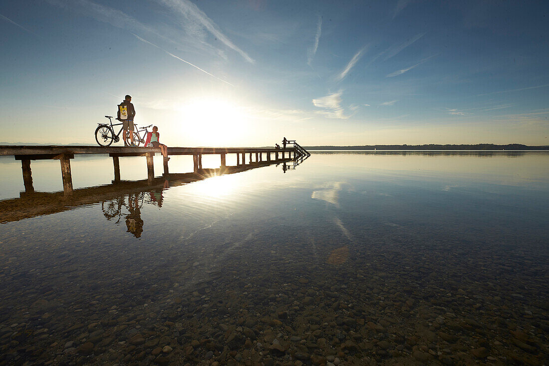 Young  woman and young man with bicycles on a jetty, Muensing, bavaria, germany