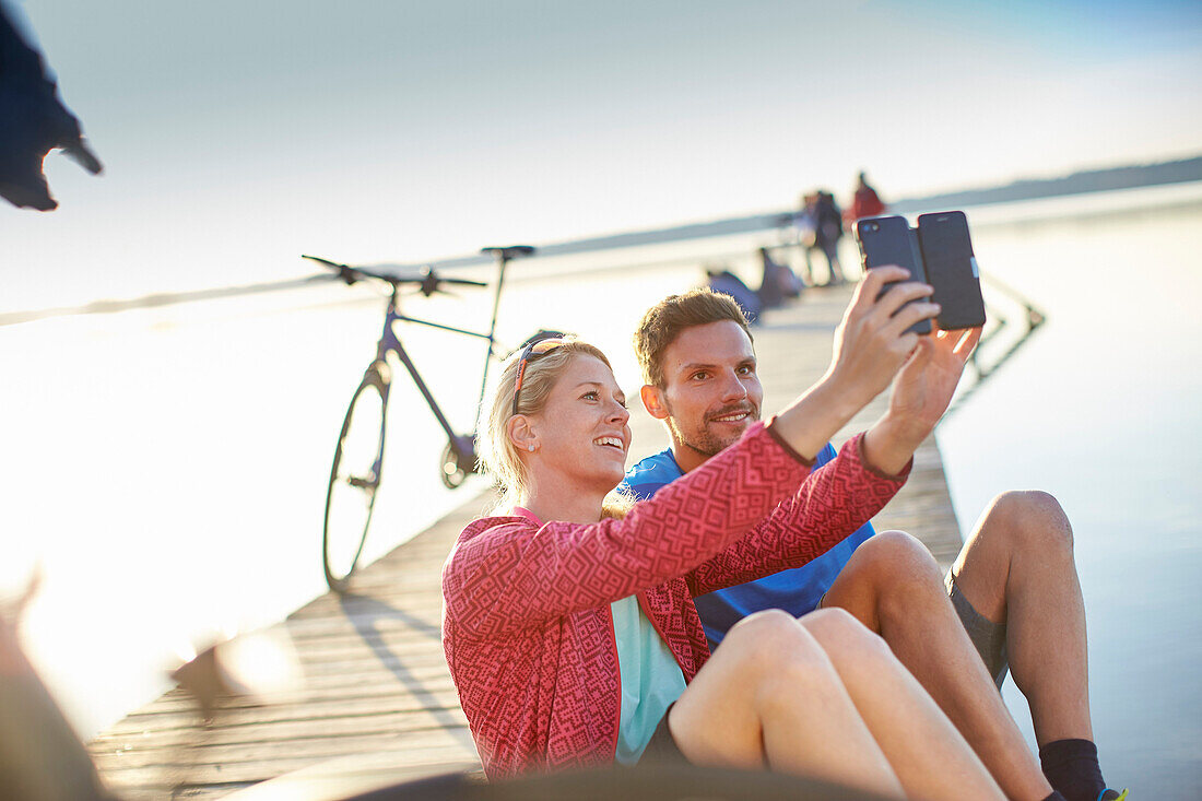 junge Frau  und junger Mann mit Fahrrädern auf Steg am Seeufer machen en Selfie, Starnberger See, Bayern, Deutschland