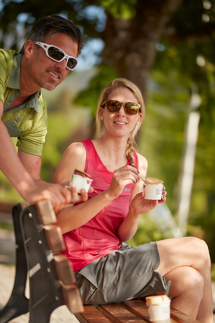 Young  woman young man having a break on bicycle tour eating icecream, Kochel, bavaria, germany