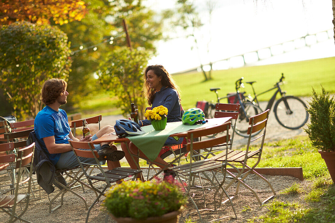 Young  woman and young man on bicycletour sitting in beergarden, Muensing, Lake Starnberg;  bavaria, germany