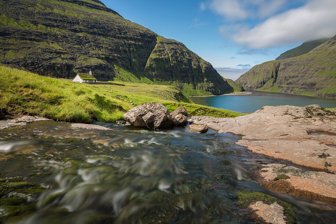 stream at the foot of a vegetal roofed church at the end of a fjord, the sea in the distance, saksun, streymoy, faroe islands, denmark