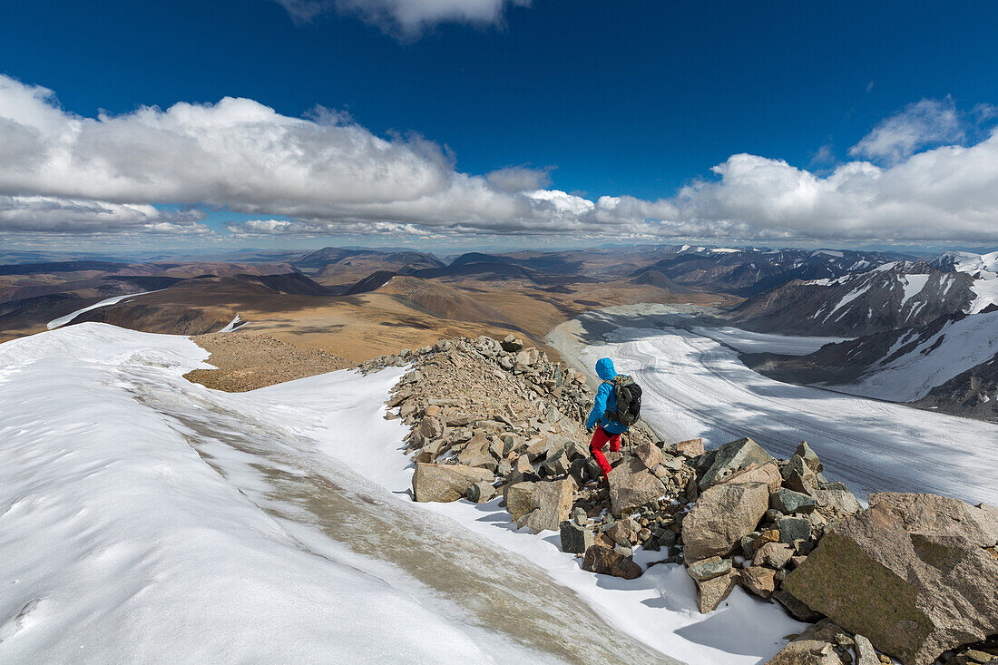hiker following the rocky crest of mount malchin, tavan bogd massif in the background, altai, bayan-olgii province, mongolia