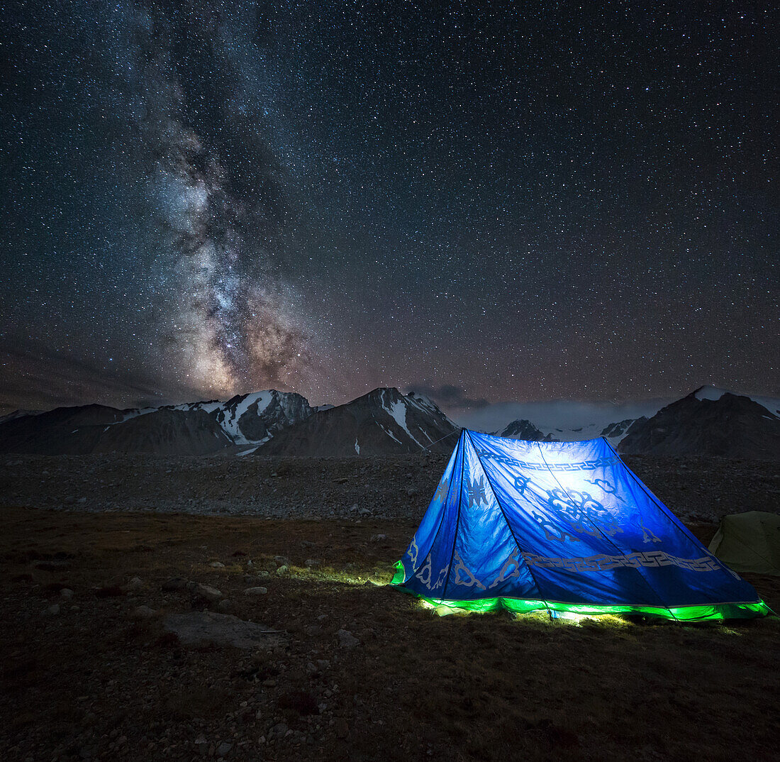 lit-up mongolian tent in front of the night sky and a luminous milky way, mount khuiten base camp, altai mountains in the background, bayan-olgii province, mongolia