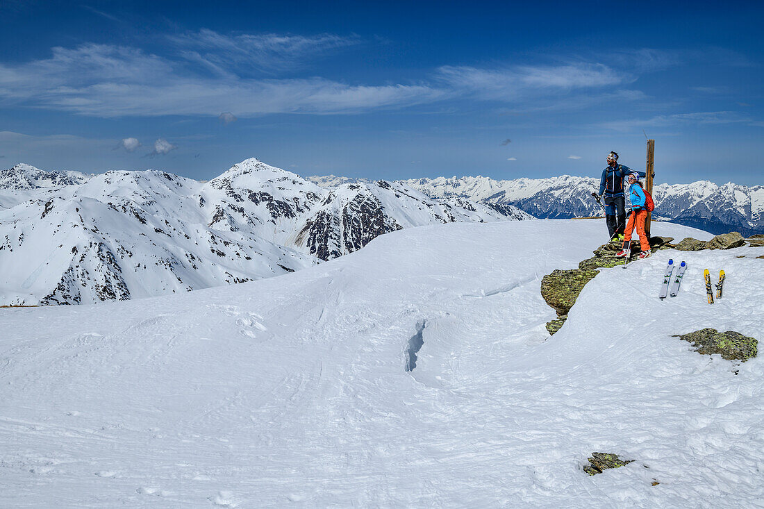 Man and woman backcountry-skiing standing at summit of Halslspitze and looking towards Tuxer Alps, Halslspitze, Tuxer Alps, Tyrol, Austria