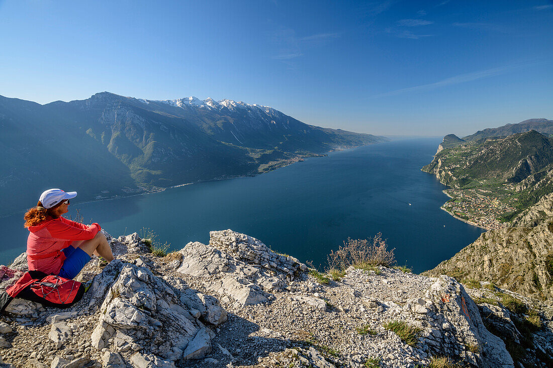 Frau beim Wandern sitzt auf Felssporn und blickt auf Gardasee und Gardaseeberge, Gardasee, Gardaseeberge, Trentino, Italien