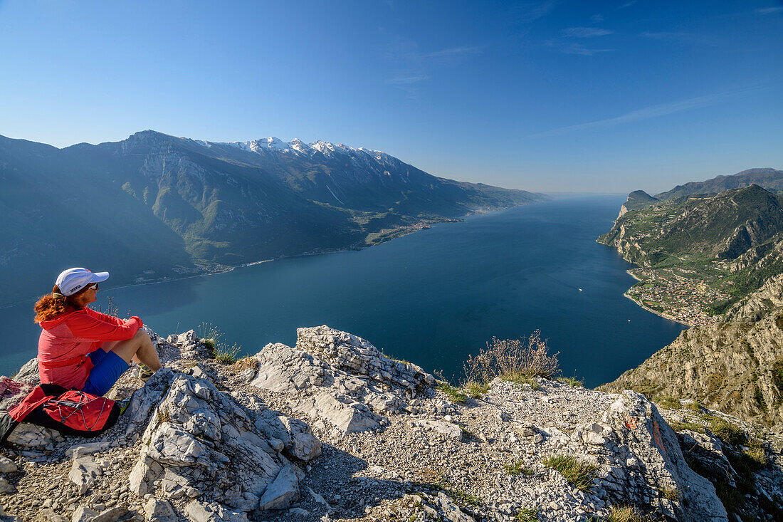 Woman hiking sitting at rock and looking towards lake Garda and Garda Mountains, lake Garda, Garda Mountains, Trentino, Italy