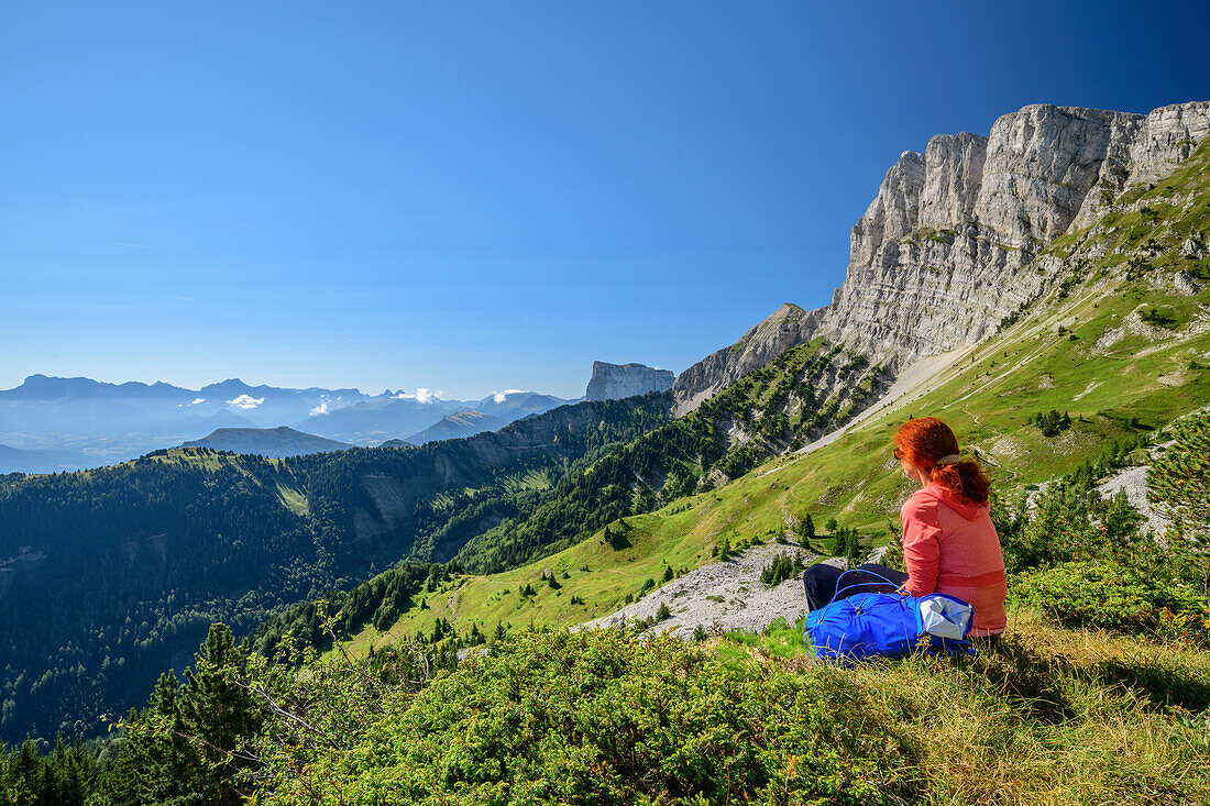Frau beim Wandern sitzt auf Wiesenabsatz und blickt auf die Bergkulisse, am Grand Veymont, Vercors, Dauphine, Dauphiné, Isère, Frankreich