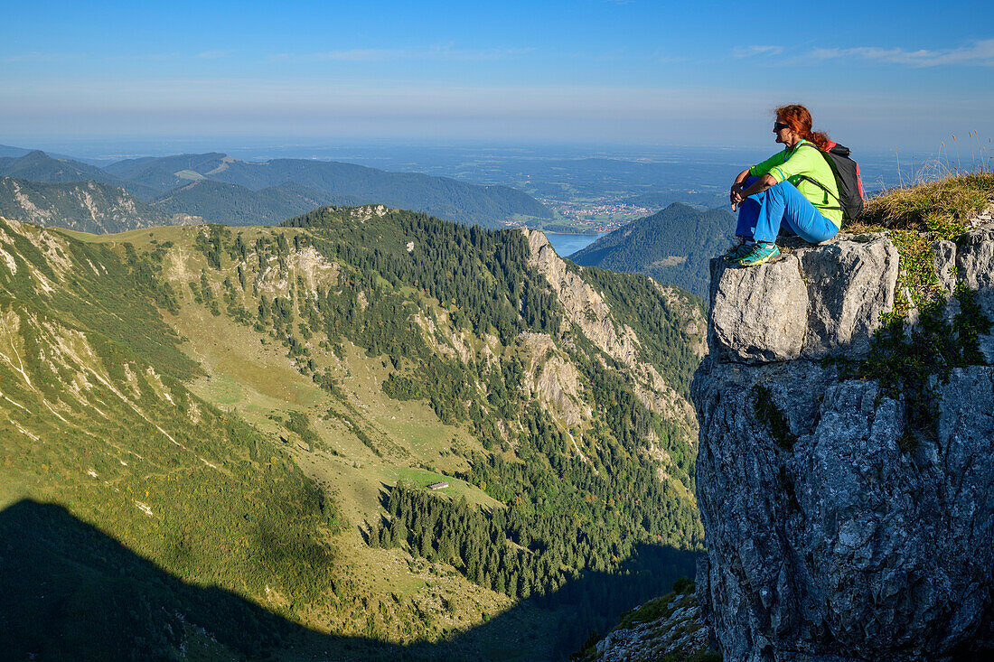 Frau beim Wandern sitzt auf Felsabsatz und blickt in die Tiefe, Aiplspitze, Mangfallgebirge, Bayerische Alpen, Oberbayern, Bayern, Deutschland