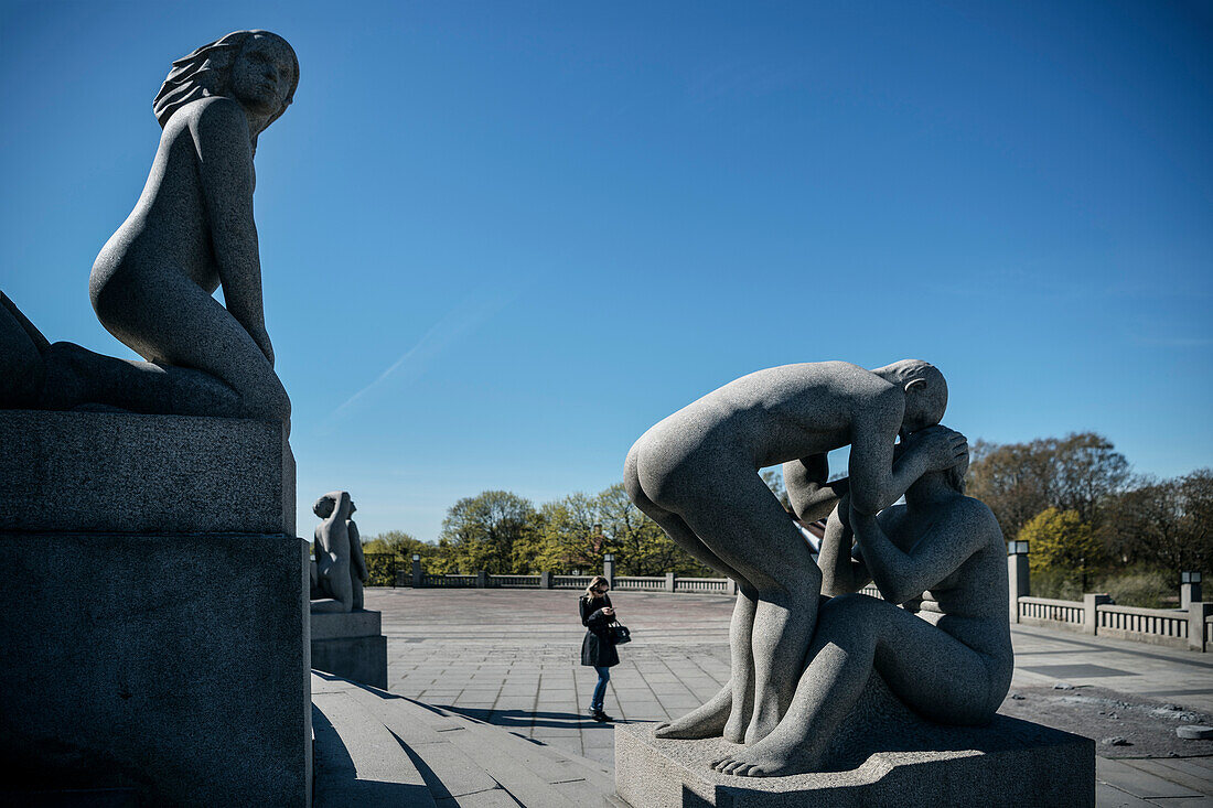woman looks at her mobile phone in between naked sculptures of Vigelandsparken, sculpture park of sculptor Gustav Vigeland, Frogner Park, Oslo, Norway, Scandinavia, Europe