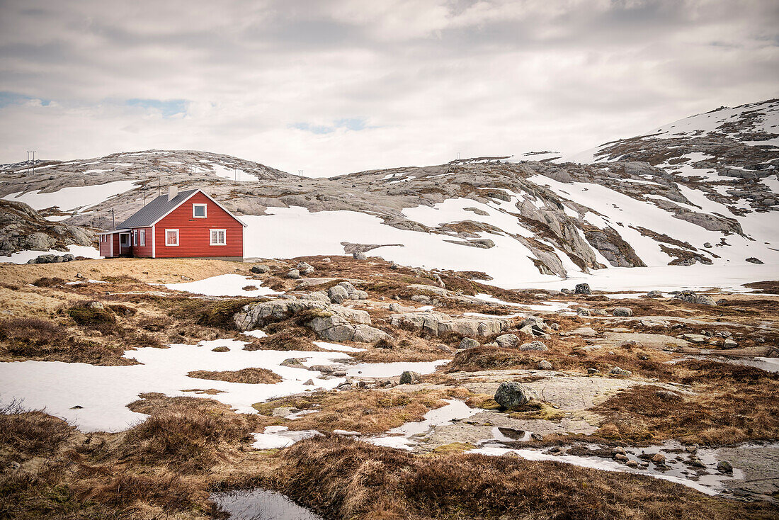 rotes Haus umgeben von Schnee und Eis am Stausee Lyngsvatnet im Hochland von Norwegen bei Lysebotn, Skandinavien, Europa