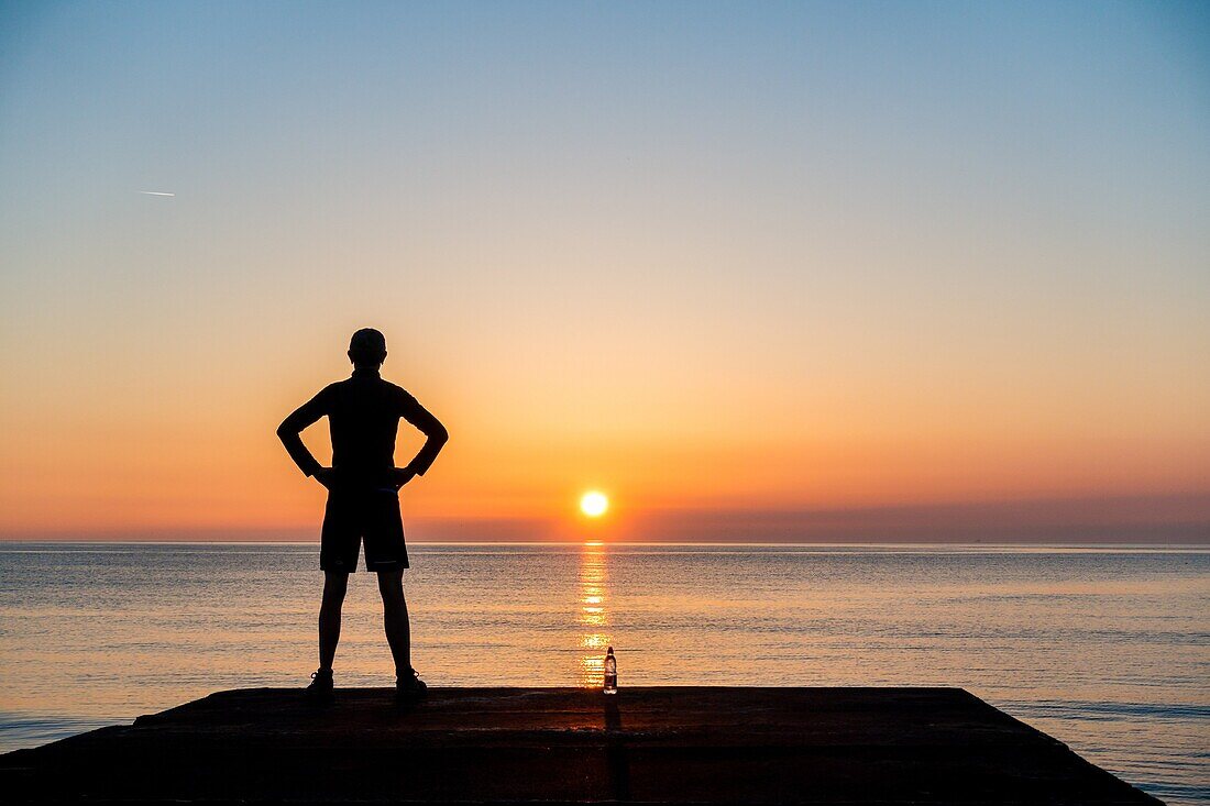 Seaton Carew, County Durham, north east England. United Kingdom. A jogger looks out over the North sea at sunrise.